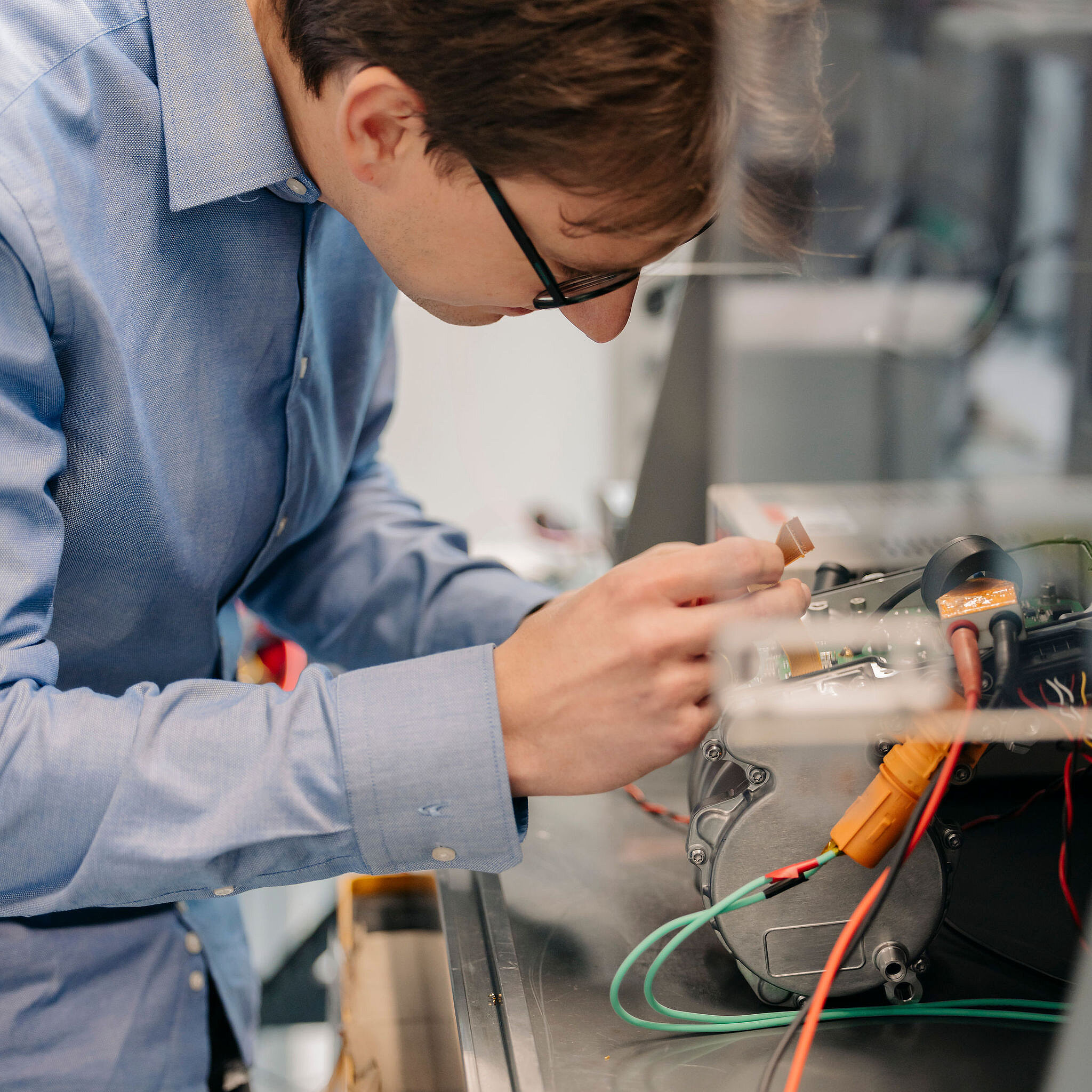 Ingenieur von Silver Atena untersucht eine elektronische Baugruppe mit Metallgehäuse und angeschlossenen Leitungen im Entwicklungslabor.