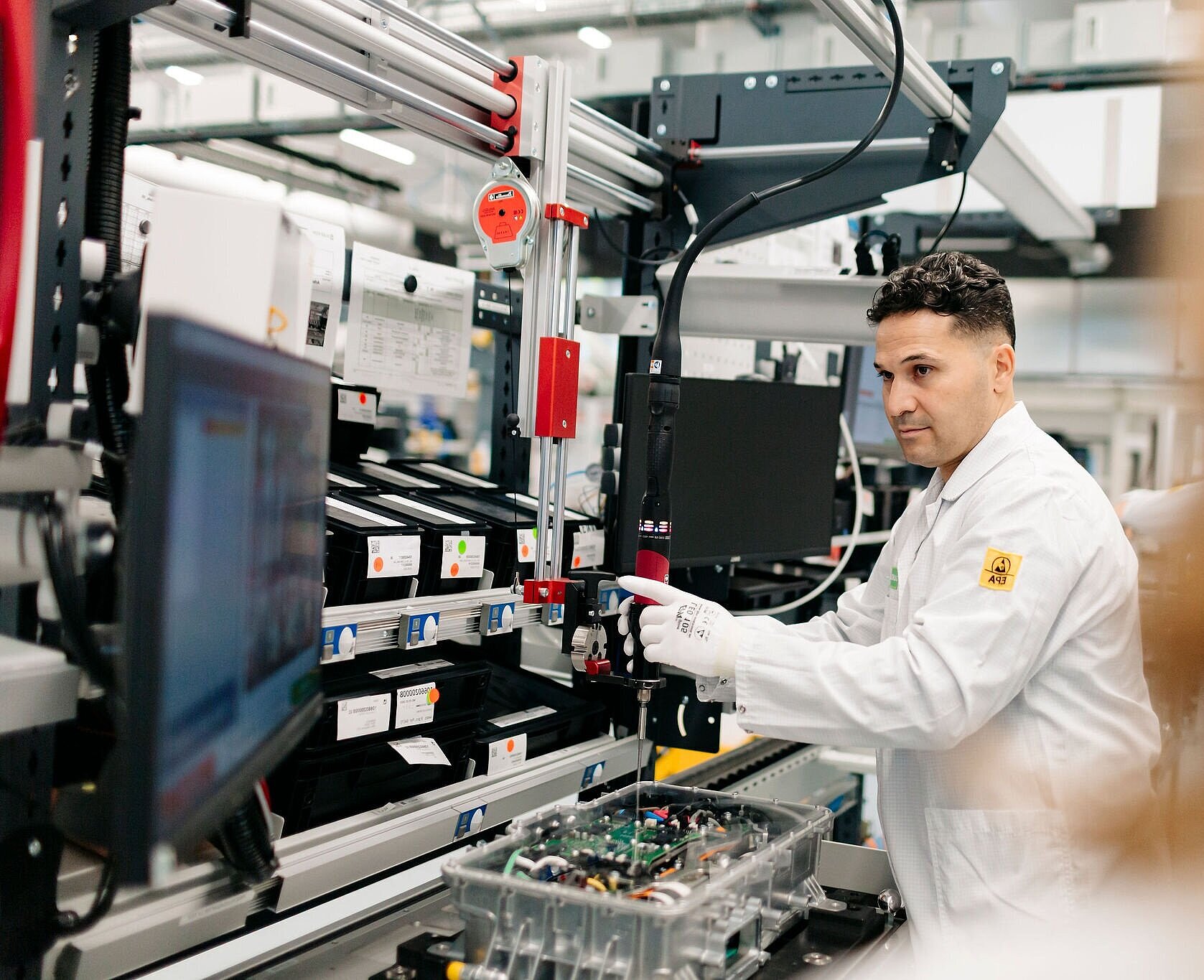 Person an einer Fertigungsstation mit elektronischer Baugruppe und Werkzeugführung.