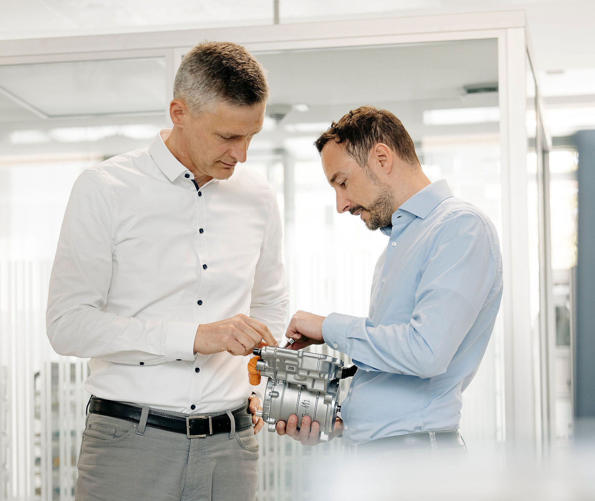 Zwei Ingenieure von Silver Atena untersuchen gemeinsam eine elektronische Antriebseinheit mit Metallgehäuse und Steckverbindern.