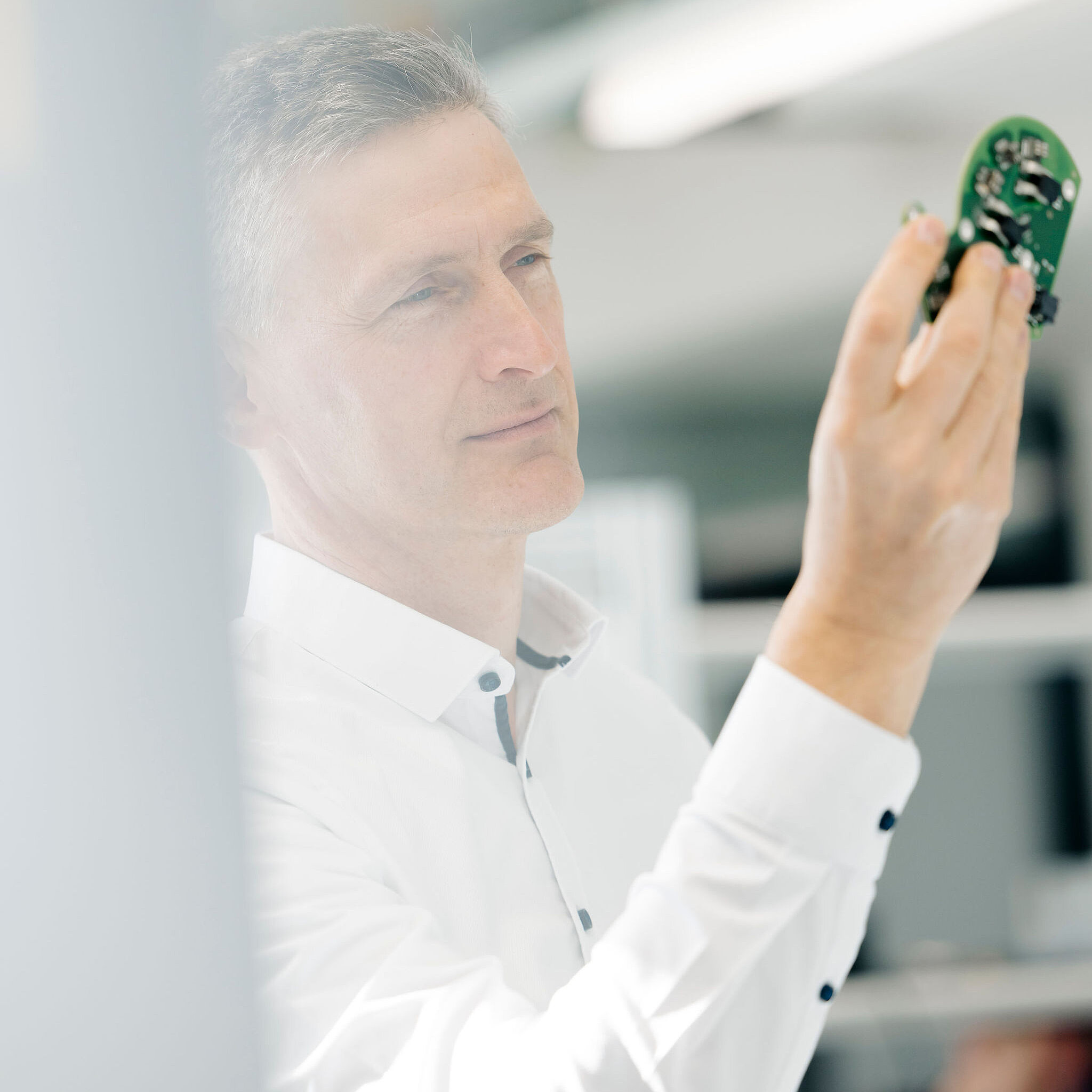 Mitarbeiter von Silver Atena kontrolliert eine bestückte elektronische Leiterplatte bei der visuellen Qualitätsprüfung.