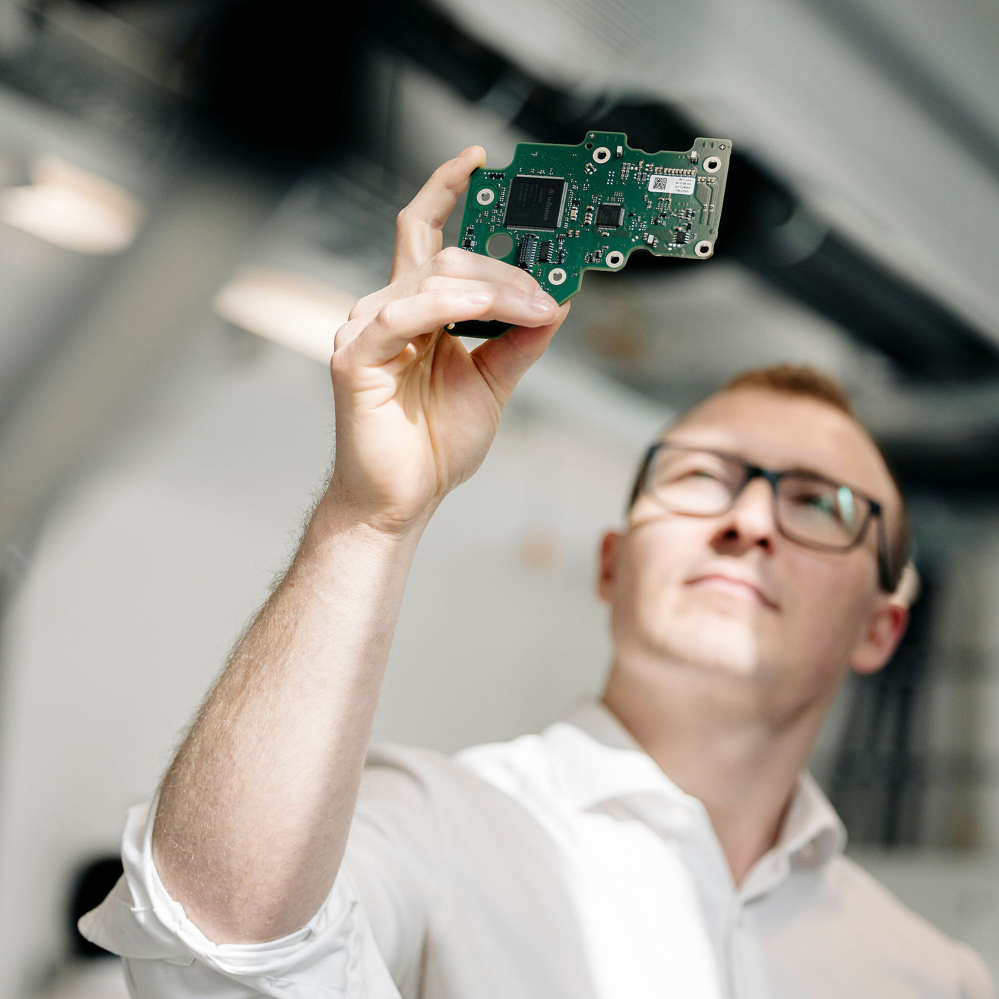 Ingenieur von Silver Atena hält eine bestückte Leiterplatte gegen das Licht und prüft die elektronischen Bauteile visuell.