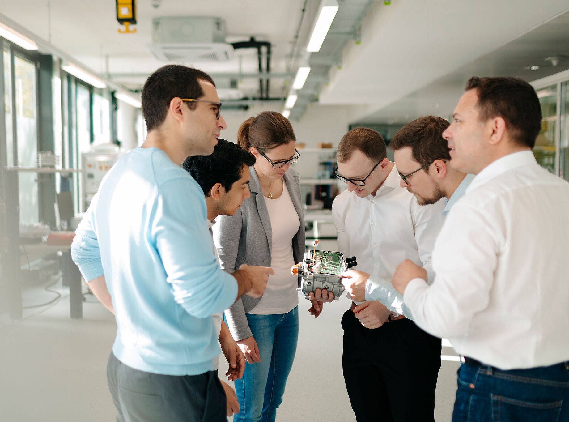 Sechs Mitarbeitende von Silver Atena besprechen die Integration einer elektronischen Leiterplatte in ein geöffnetes Steuergerätegehäuse.