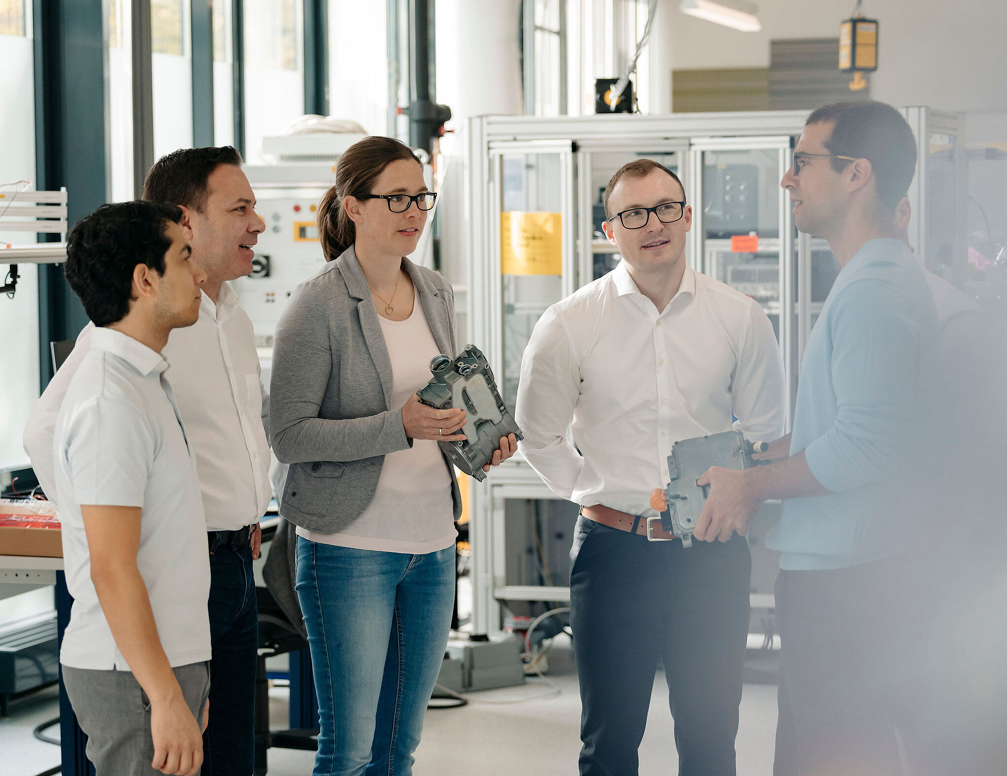 Fünf Mitarbeitende von Silver Atena besprechen elektronische Baugruppen und Gehäusekomponenten gemeinsam im Entwicklungslabor.