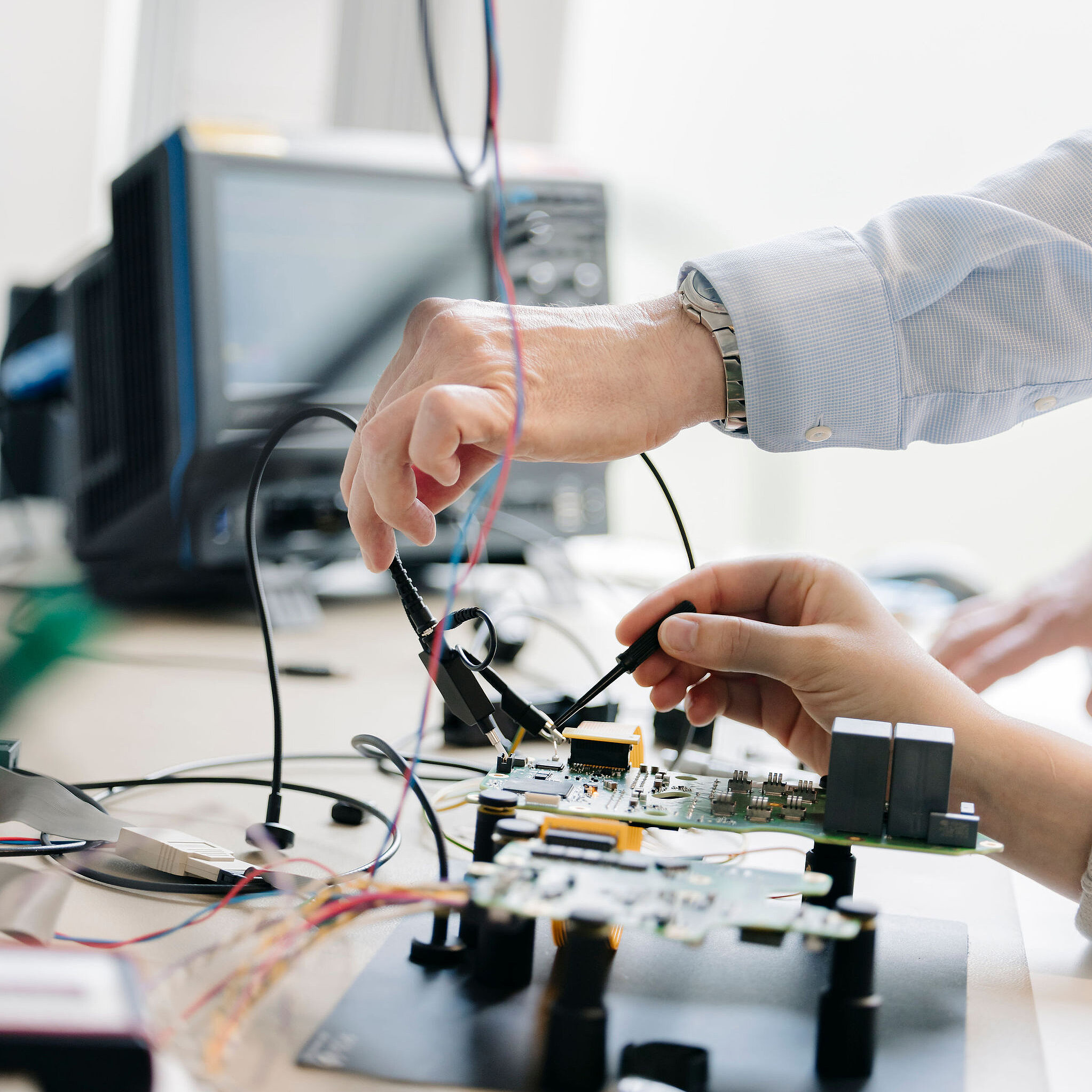 Zwei Mitarbeitende von Silver Atena prüfen eine elektronische Leiterplatte mit Messsonden an einem Laborarbeitsplatz.