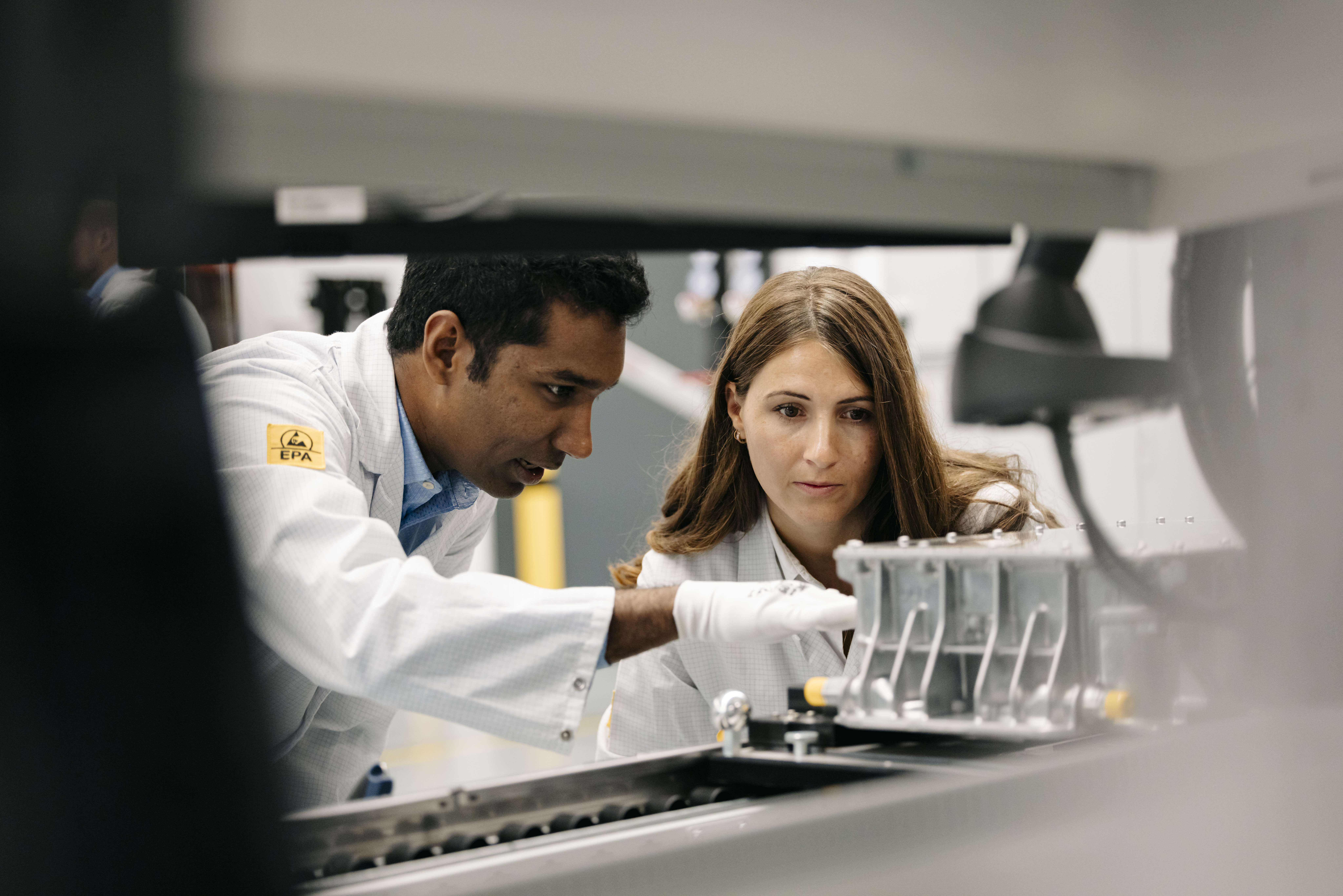 Zwei Personen prüfen ein elektronisches Bauteil in einer technischen Testumgebung.