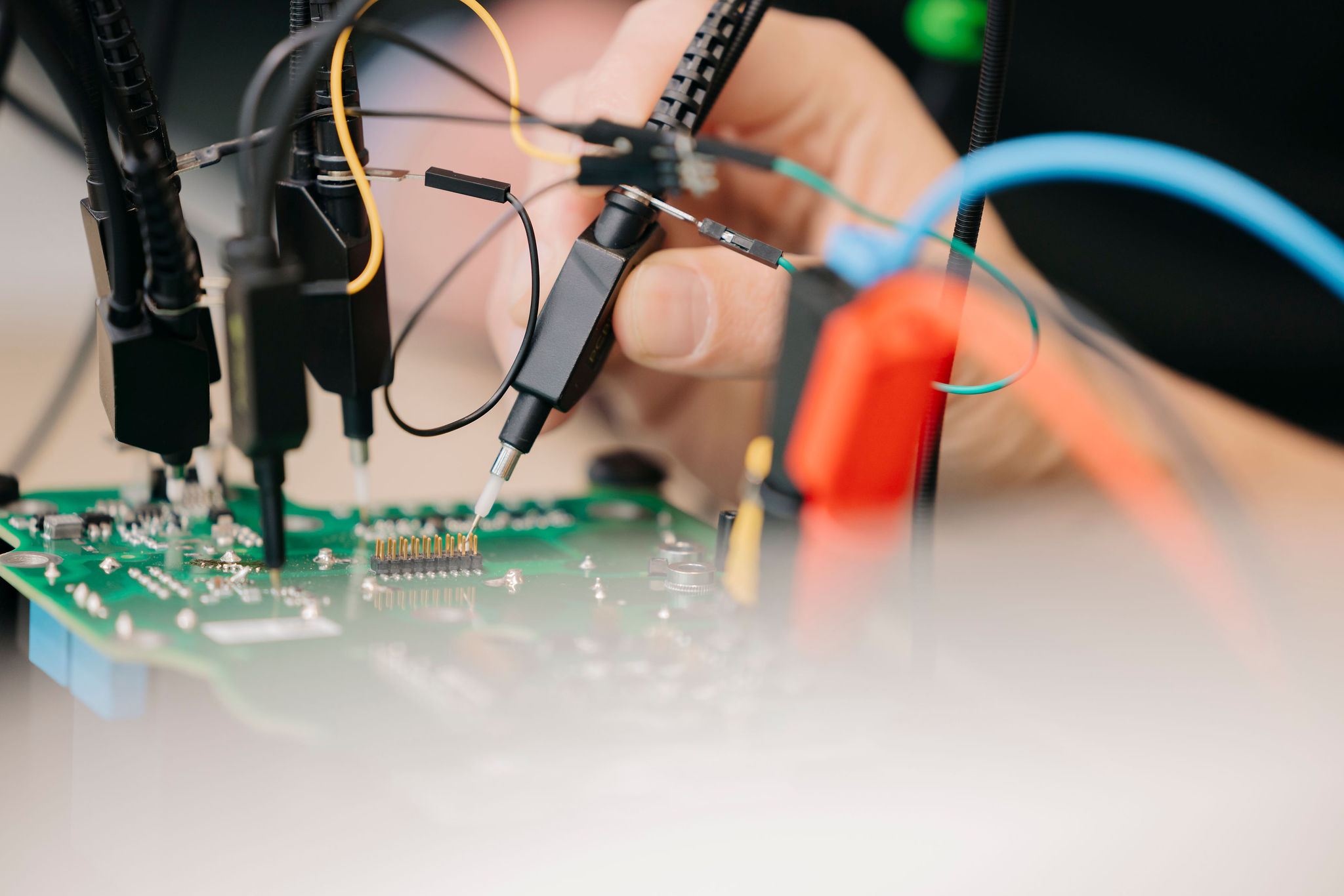 Detailaufnahme einer elektronischen Leiterplatte während der Prüfung mit mehreren Messspitzen und angeschlossenen Prüfleitungen.