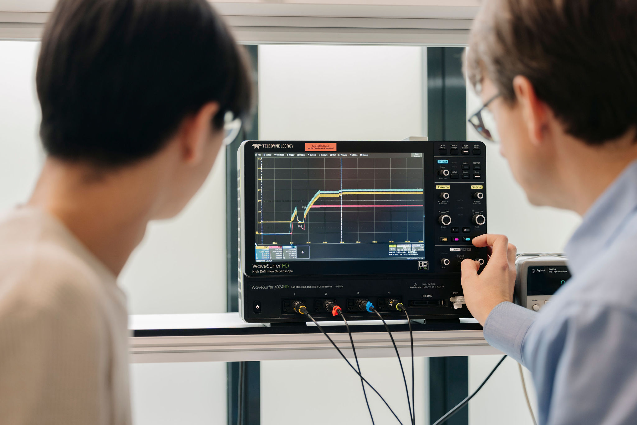Zwei Ingenieure analysieren elektrische Signalverläufe auf einem Oszilloskop im Elektroniklabor