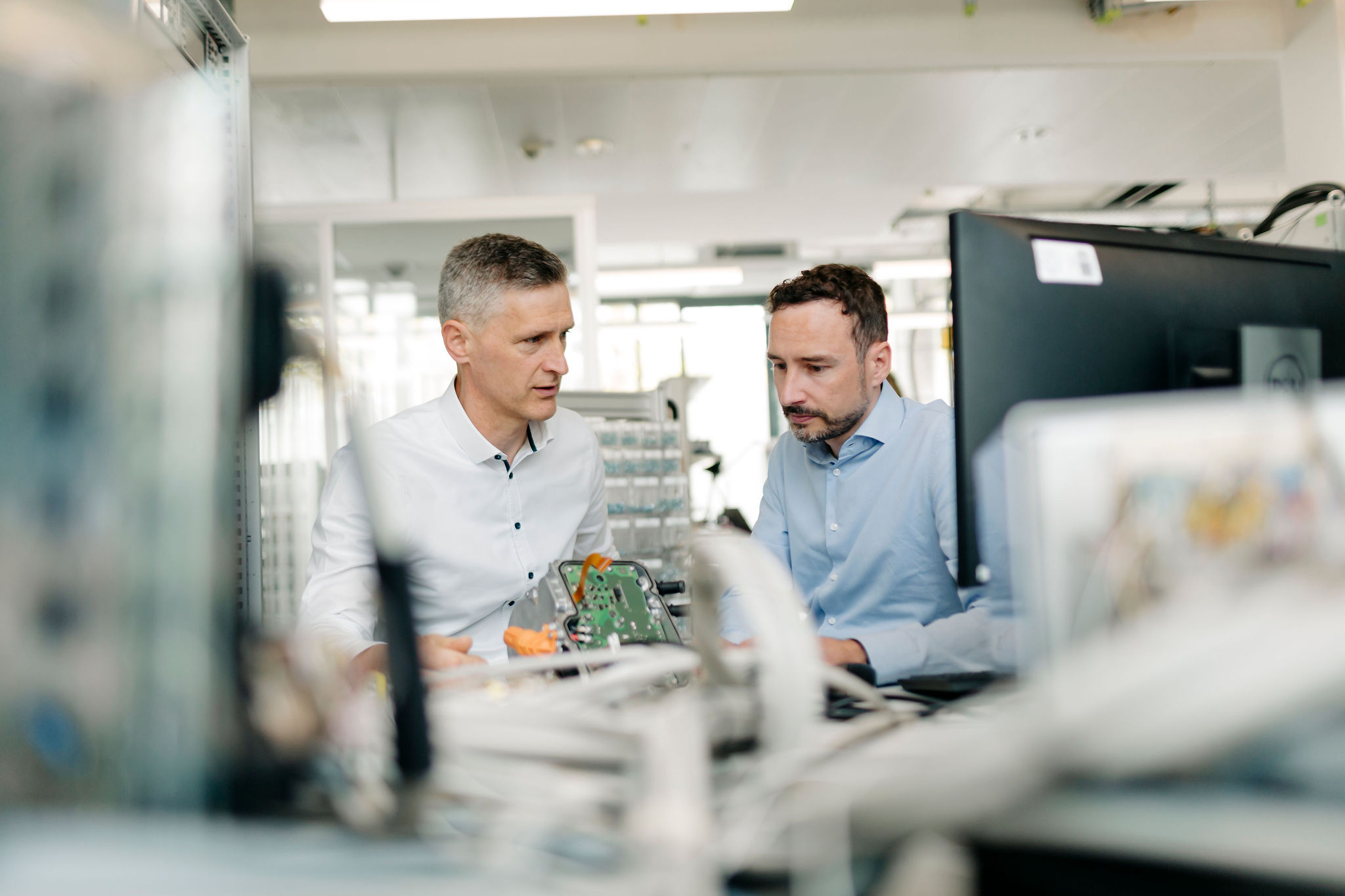 Zwei Ingenieure untersuchen eine elektronische Baugruppe mit Leiterplatte an einem Entwicklungsarbeitsplatz