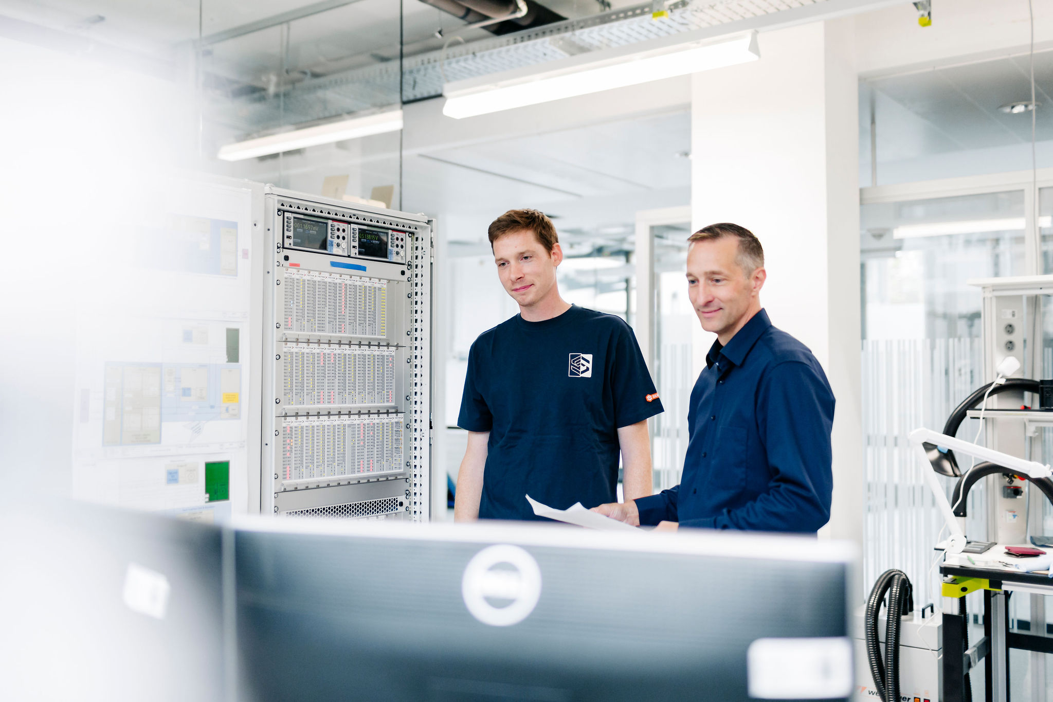 Zwei Mitarbeiter von Silver Atena überprüfen technische Unterlagen und Messdaten an einem modularen Prüfstand im Entwicklungslabor.
