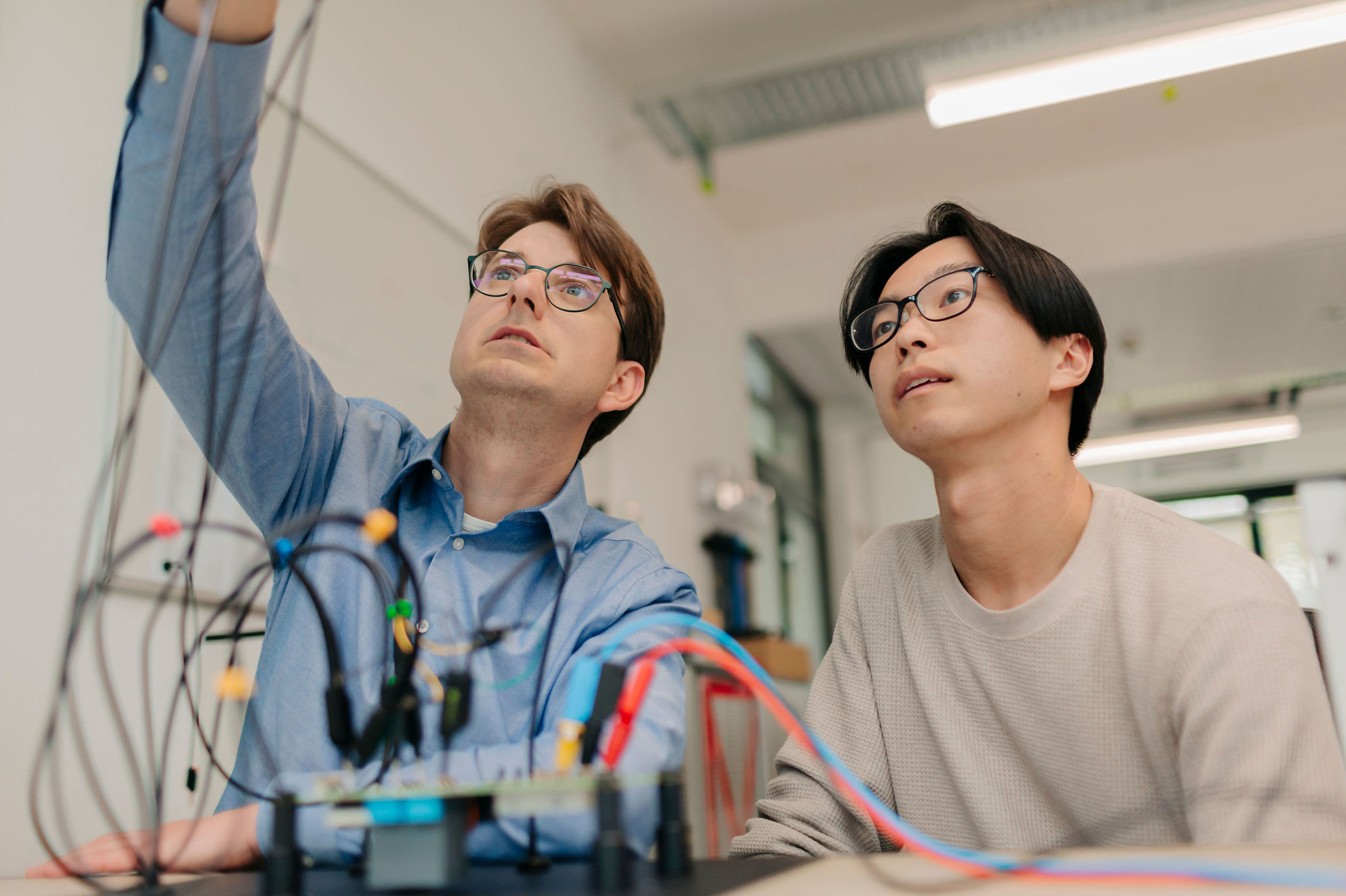 Zwei Ingenieure analysieren einen technischen Versuchsaufbau mit Messleitungen und elektronischen Komponenten im Entwicklungslabor.