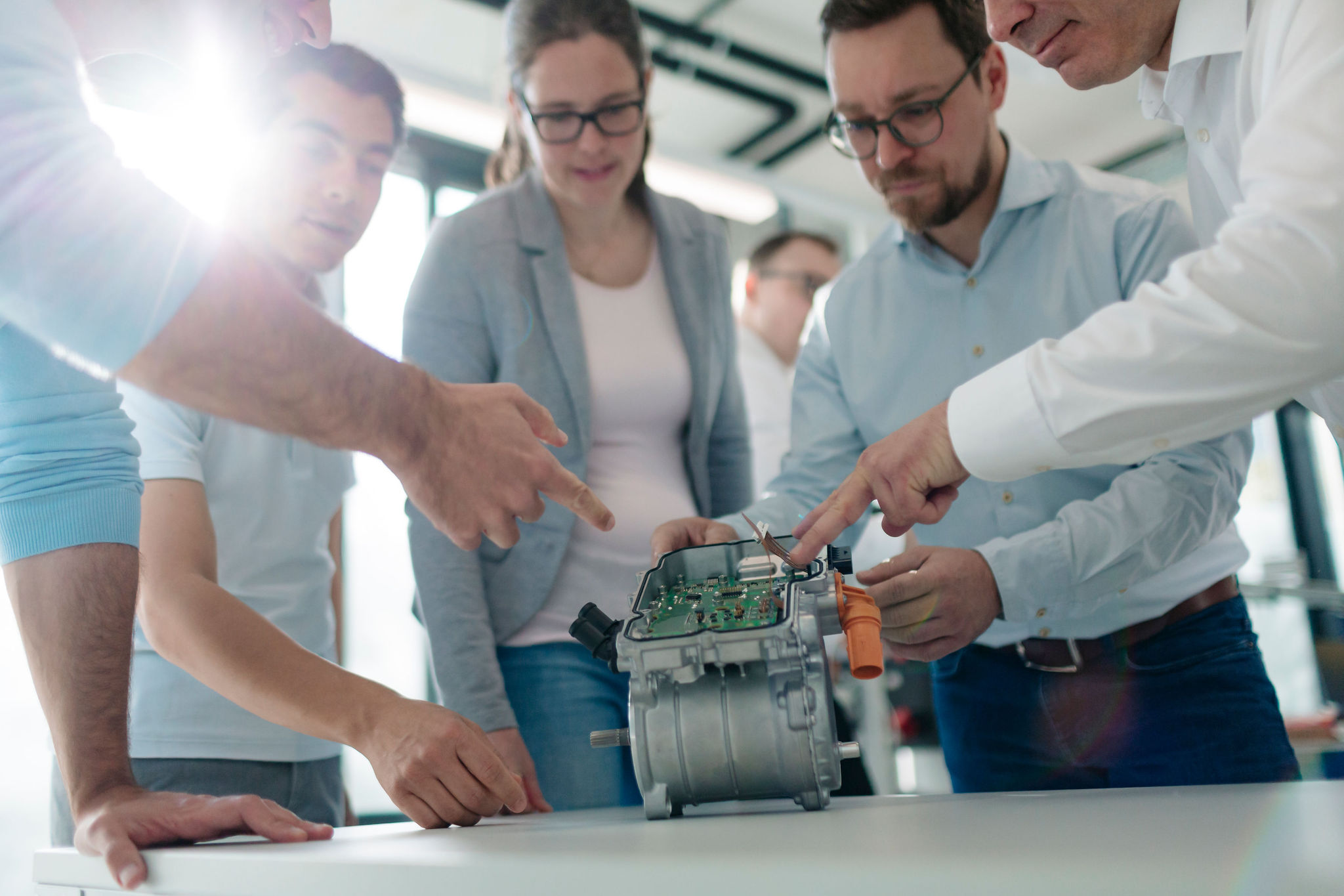 Fünf Mitarbeitende von Silver Atena begutachten gemeinsam eine geöffnete elektronische Baugruppe mit Leiterplatte und Metallgehäuse.
