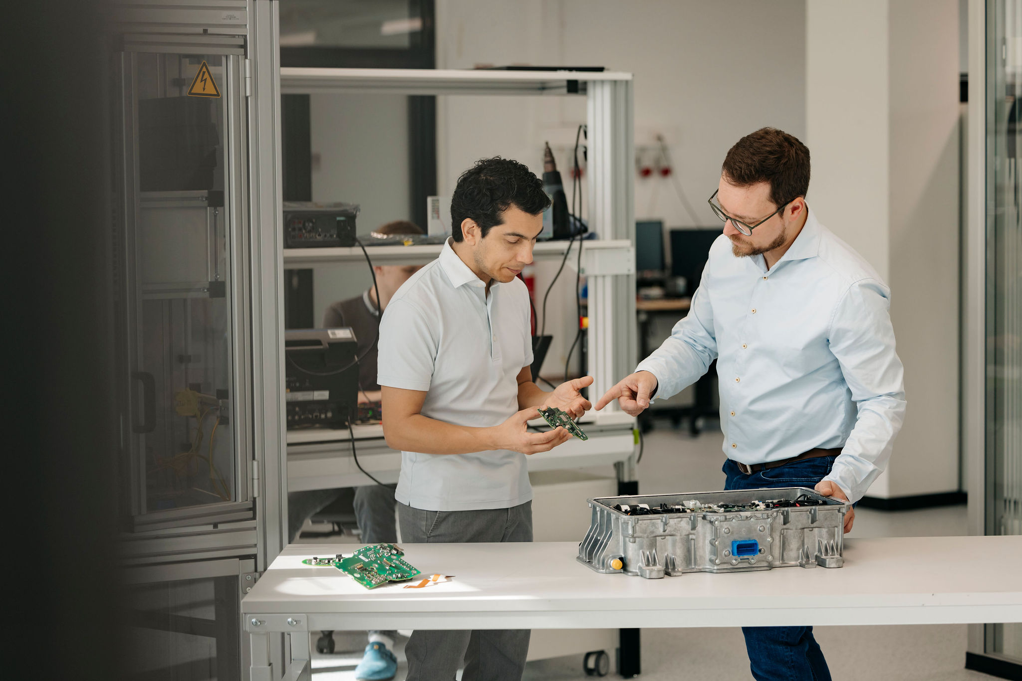 Zwei Ingenieure von Silver Atena besprechen eine elektronische Leiterplatte und ein geöffnetes Steuergerätegehäuse im Entwicklungslabor.