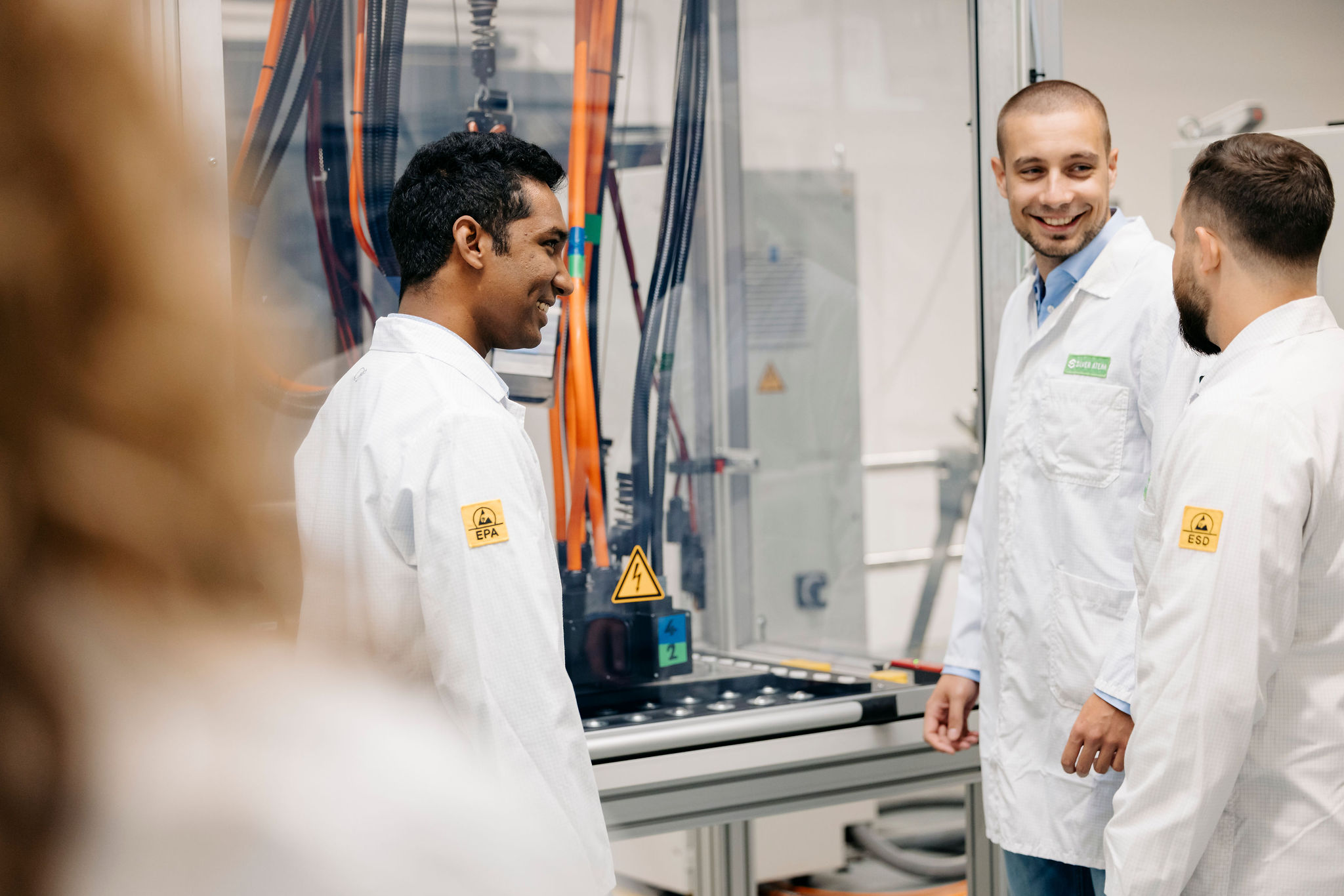 Drei Mitarbeiter von Silver Atena im Austausch an einer industriellen Prüfanlage mit Hochvolt-Komponenten und Messleitungen.