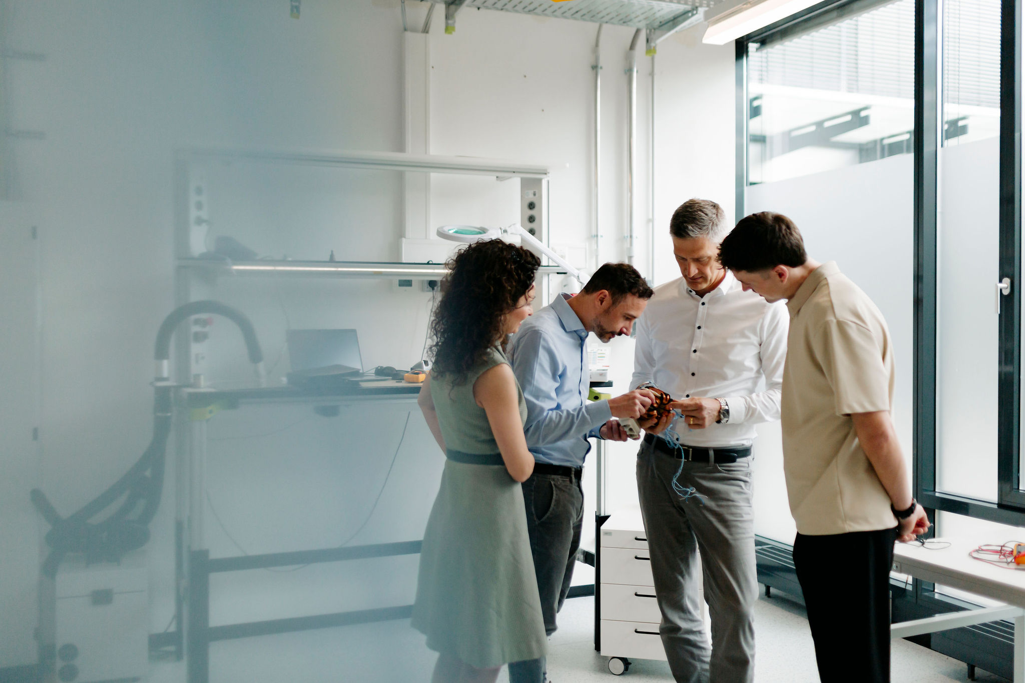 Vier Mitarbeitende von Silver Atena untersuchen gemeinsam eine elektronische Baugruppe mit Steckverbindern im Entwicklungslabor.