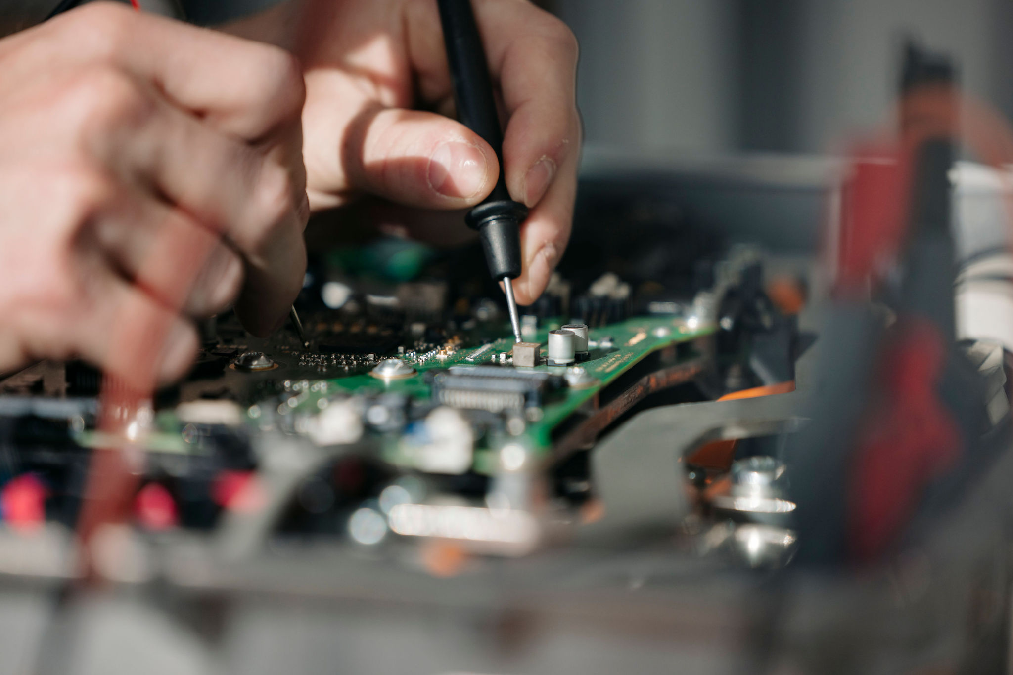 : Detailaufnahme einer elektronischen Leiterplatte während der Prüfung mit einer Messspitze an einem Bauteil.
