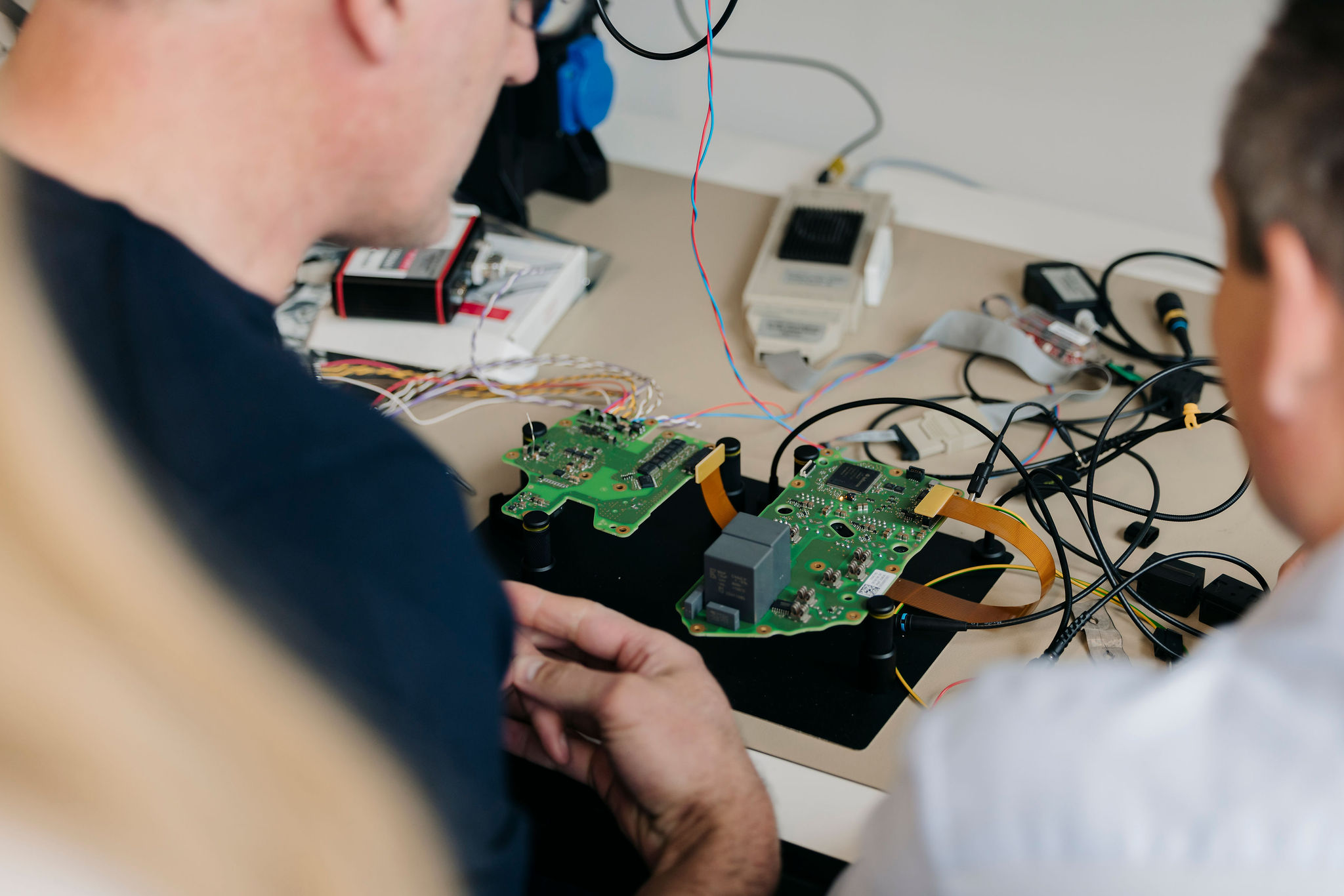 Zwei Ingenieure von Silver Atena untersuchen bestückte Leiterplatten mit angeschlossenen Messleitungen an einem Laborprüfstand.