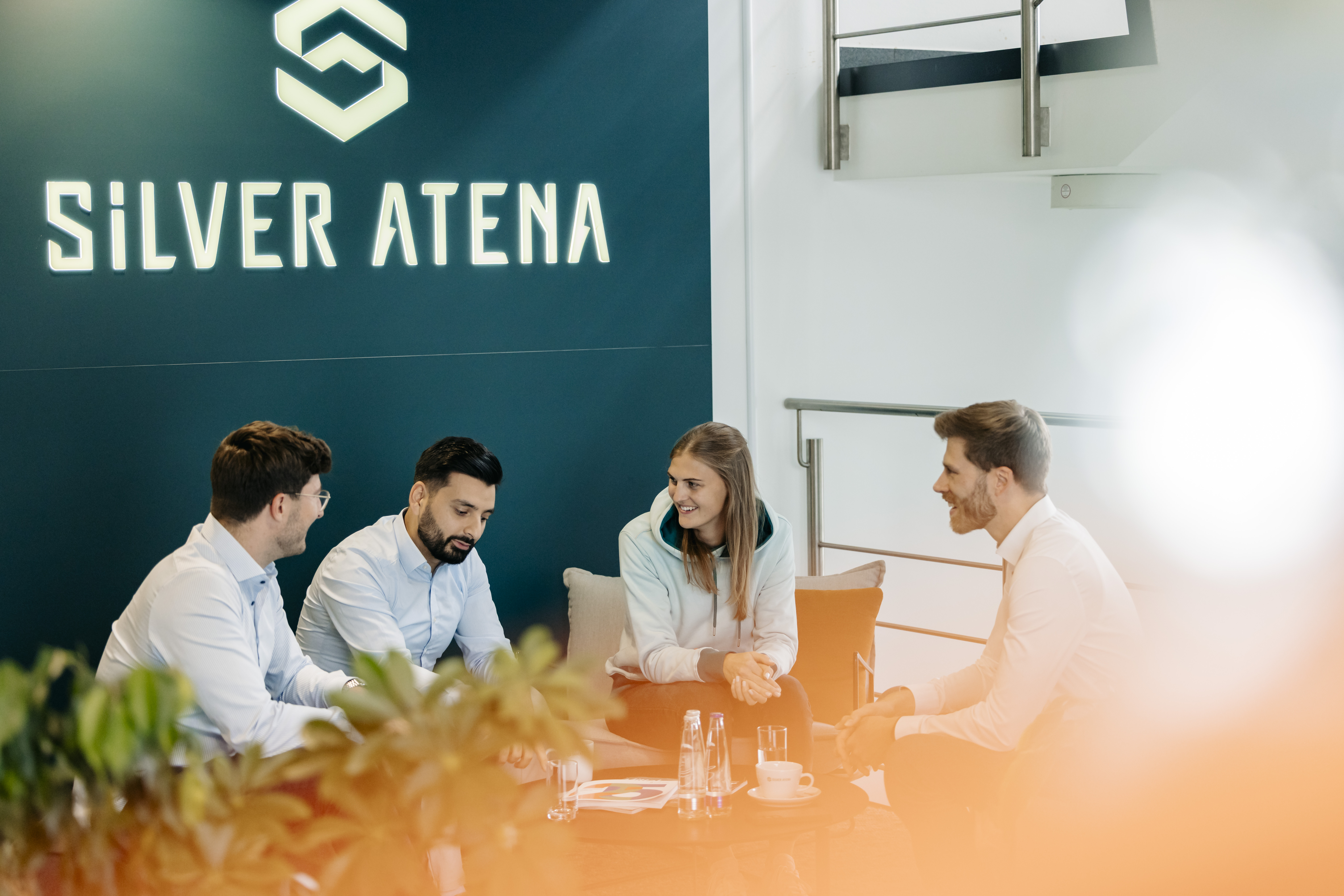 Personen sitzen auf Couch vor Wand mit Silver-Atena-Logo.