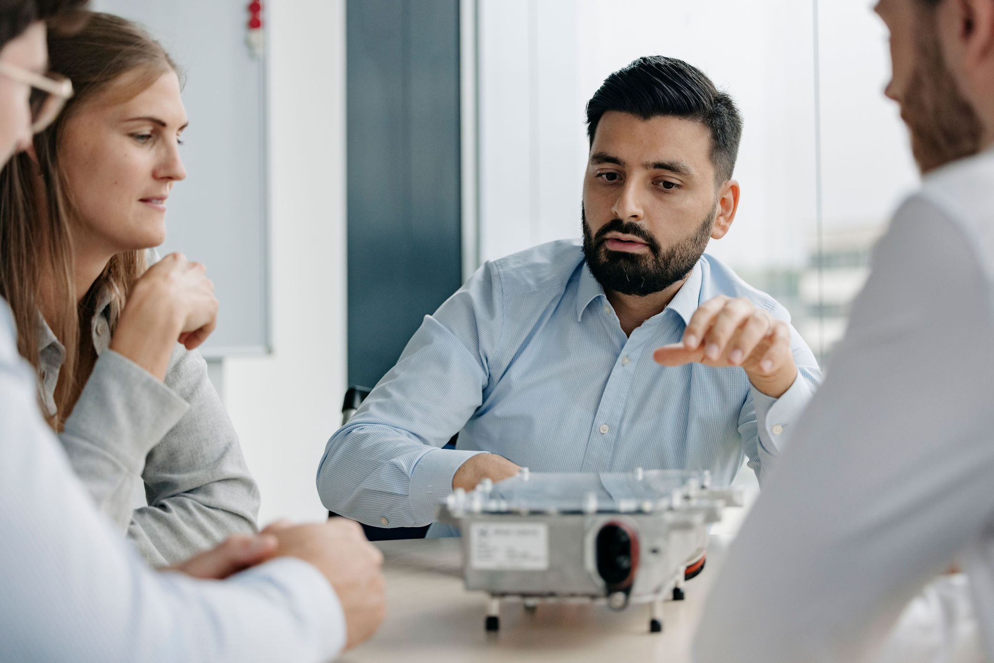 Gruppe in einer Besprechung mit einer elektronischen Baugruppe auf dem Tisch.
